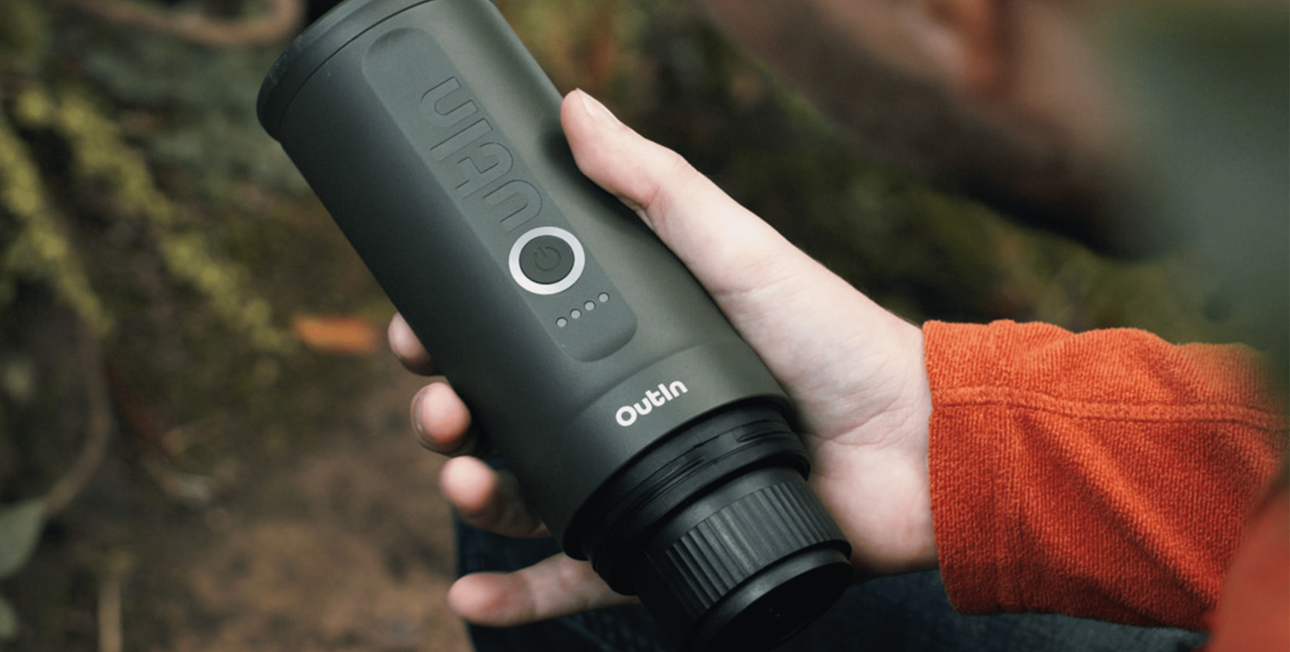 Hand holding Outin Nano Portable Espresso Machine outdoors, displaying power button and battery indicator